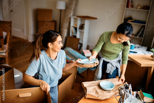 Photos Happy female friends unpacking their belongings while moving into new home
