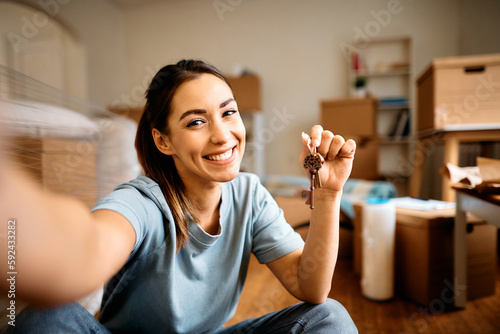 Cuadro en lienzo Young happy woman takes selfie while holding key of her new apartment and looking at camera