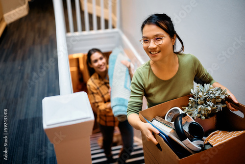 Happy Asian woman and her friend walking upstairs through hallway while moving in new apartment. photo