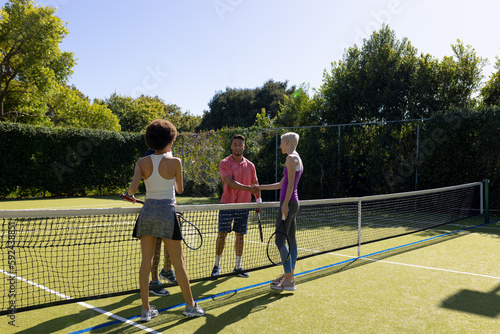 Happy diverse group of friends playing tennis, shaking hands at tennis court