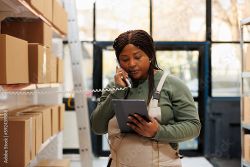 Foto Stockroom employee talking at landline phone with client while checking online order on tablet computer