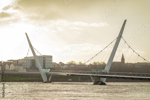 Panorama of peace bridge in Derry or Londonderry spanning across the river on a sunny spring day. Beautiful modernist bridge to the derry old town, evening feeling.