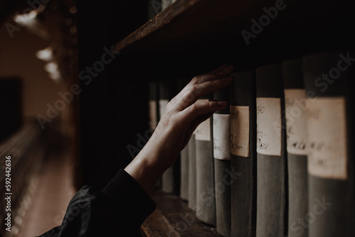 A girl picking an antique book on a shelf of a reading room in a library with her pale hand. Concept of classic literature, reading, literacy, and knowledge.
