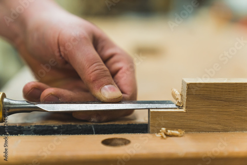 Extreme closeup shot of carpenter's hands using chisel on wooden plank. Blurred background. Woodworking and craftsmanship. High quality photo