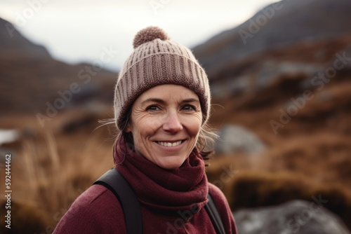 Portrait of a smiling woman with hat and backpack standing in the mountains © Robert MEYNER