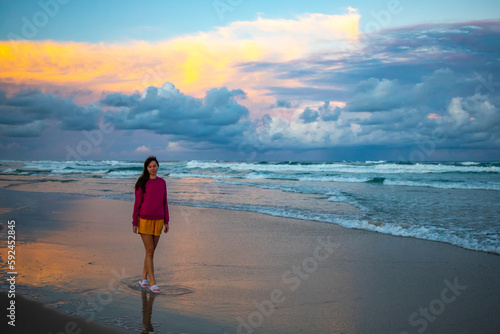 Fotobehang Beautiful girl in pink blouse walks on stunning vast Patchs beach near Byron Bay and admires colorful cloudy sunset
