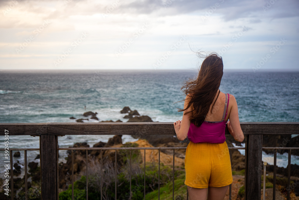 Beautiful long-haired girl stands admiring the magnificent rocky coastline and beaches in the famous Byron Bay, New South Wales, Australia