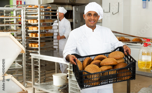 Portrait of male baker holding plastic crate with freshly baked bread in bakery