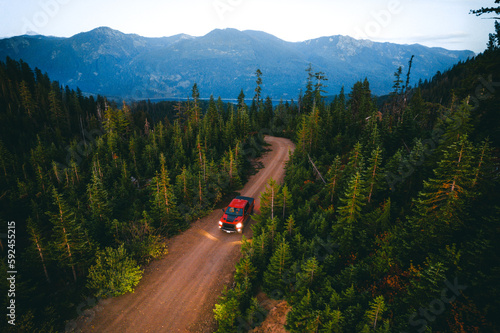 Aerial shot of shot of a pickup truck driving through the forest in the dusk in front of Cascade mountains in Washington state. photo
