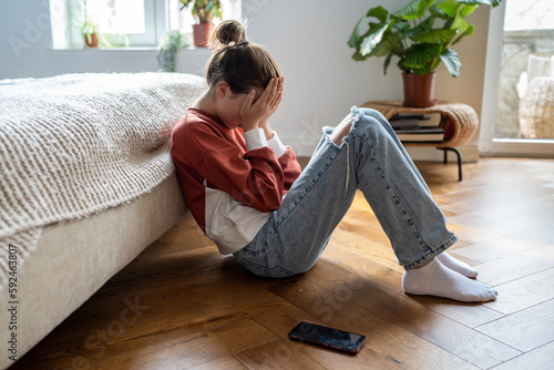 Canvastavla Unhappy teen girl covering face with hands and crying while sitting on floor with mobile phone nearby, upset frustrated child teenager being bullied or harassed online