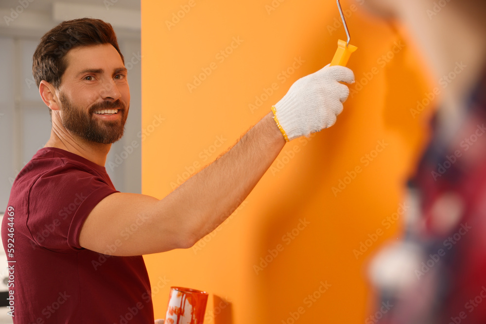 Happy designer painting orange wall with roller Happy designer painting orange wall with roller