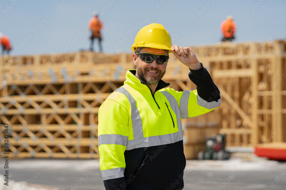 Construction worker at house under construction. Builder in building uniform on construction background. Builder at the construction site. American worker with helmet. Bilder in hardhat. Construction worker at house under construction. Builder in building uniform on construction background. Builder at the construction site. American worker with helmet. Bilder in hardhat.