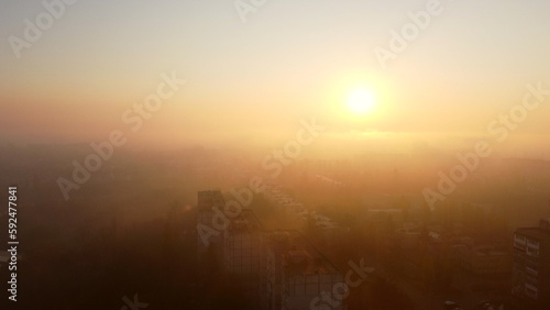 Dawn Sunrise in city scene. Bright shining sun at dawn  fog over rooftops of multi-storey buildings. Top view of many houses town. Landscape. Cityscape  urban scenery. Aerial drone view.