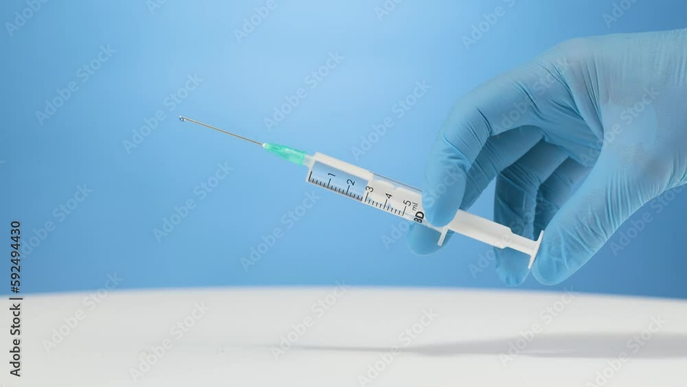 Medical gloves hand injecting vaccination liquid with syringe, blue background Medical gloves hand injecting vaccination liquid with syringe, blue background