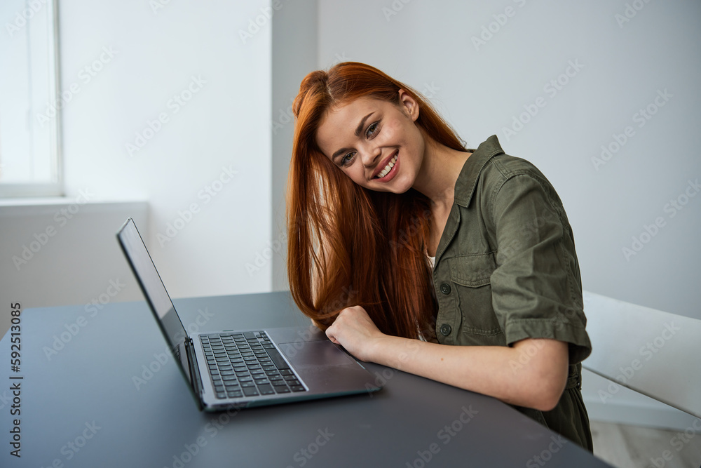 portrait of a cute, smiling red-haired woman sitting at a laptop in a bright room portrait of a cute, smiling red-haired woman sitting at a laptop in a bright room
