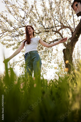 joyful woman stands against the background of a flowering tree in summer clothes