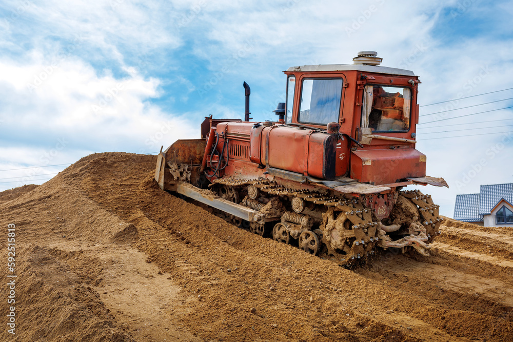 An old orange bulldozer performs work to level the sandy soil An old orange bulldozer performs work to level the sandy soil