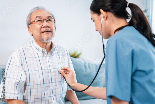 Картината върху платно Caring young female doctor examining her contented senior patient with stethoscope in living room