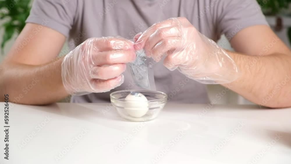 A man puts disposable plastic transparent gloves on his hands to dye Easter eggs. Coloring of Easter eggs. A man puts disposable plastic transparent gloves on his hands to dye Easter eggs. Coloring of Easter eggs.