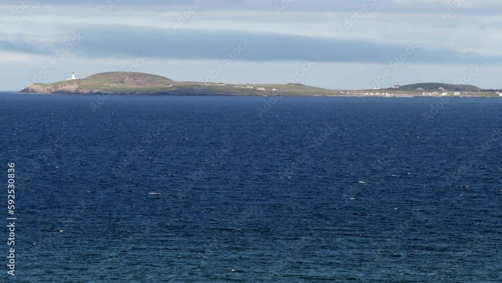 Telephoto shot of the headland of the Point peninsula. The Tiumpan head lighthouse is visible. In the background is the inlet of Broadbay near Stornoway, part of the Outer Hebrides of Scotland. Telephoto shot of the headland of the Point peninsula. The Tiumpan head lighthouse is visible. In the background is the inlet of Broadbay near Stornoway, part of the Outer Hebrides of Scotland.