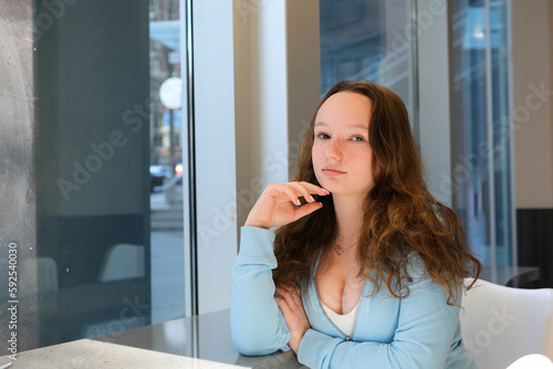 young schoolgirl teenager sitting by the window in the classroom studying offline school institute white classroom large windows blue blouse loose hair