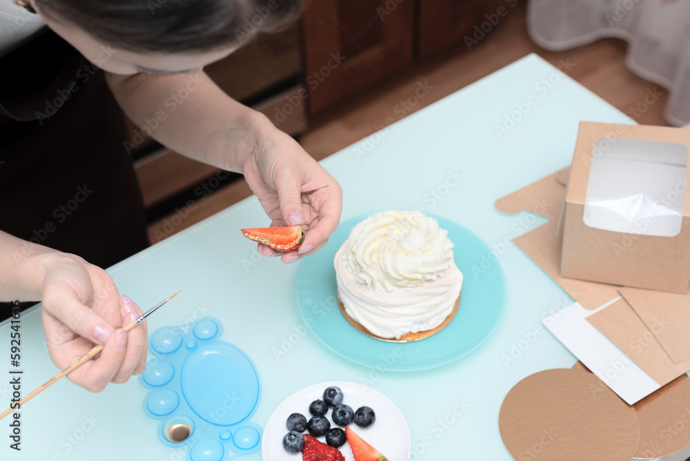 Woman pastry chef at home decorating homemade meringue cake Pavlova with summer fresh berries with selective focus. Homemade pastry, delicious sweets concept Woman pastry chef at home decorating homemade meringue cake Pavlova with summer fresh berries with selective focus. Homemade pastry, delicious sweets concept