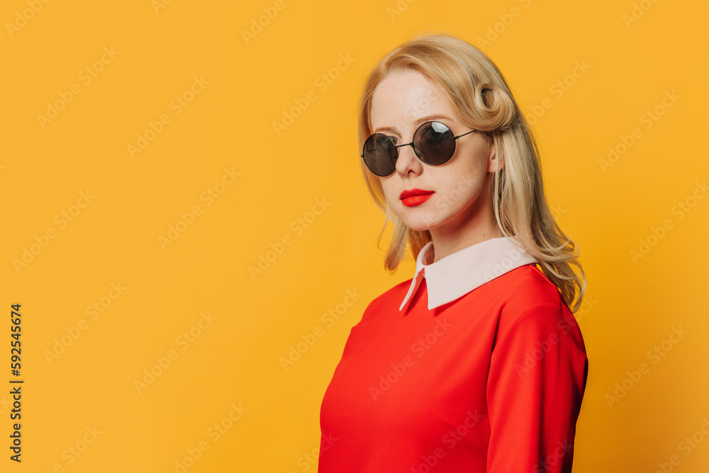 Stylish serious blonde hair woman in red dress and sunglasses on yellow background Stylish serious blonde hair woman in red dress and sunglasses on yellow background