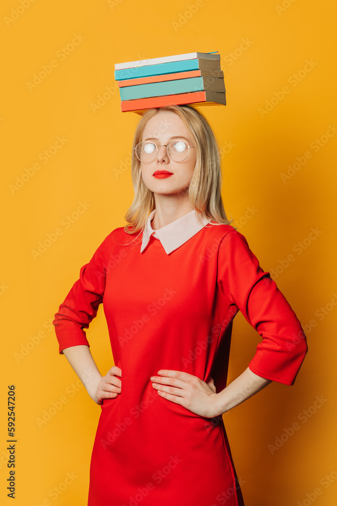 Stylish blond hair woman in glasses and red dress with book on head on yellow background Stylish blond hair woman in glasses and red dress with book on head on yellow background