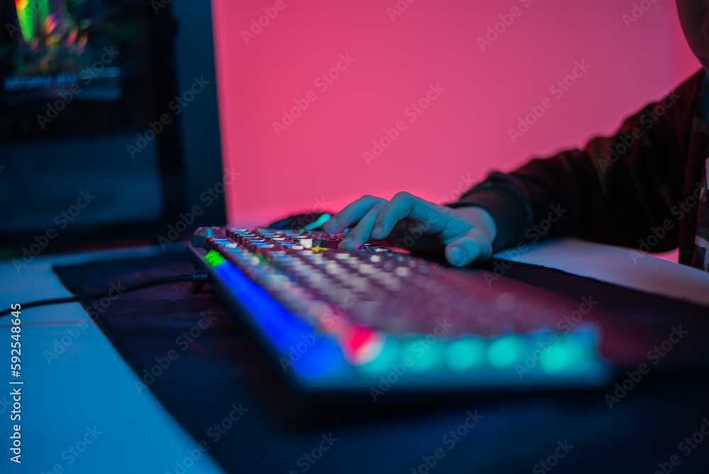 Close-up On Gamer's Hands on a keyboard, Actively Pushing Buttons, Playing MMO Games Online. Background is Lit with Neon Lights. Close-up On Gamer's Hands on a keyboard, Actively Pushing Buttons, Playing MMO Games Online. Background is Lit with Neon Lights.