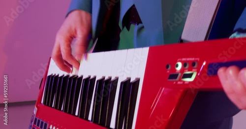 Musician with red keytar in hands playing in band on concert in club, hands close-up. Man dances to the rhythm of music. Musical performance, play in group, enjoying working artist on stage concept.  photo