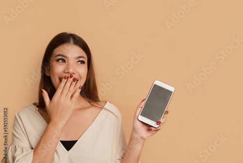 Portrait of beautiful Asian a woman showing smartphone standing over beige background, copy space.
