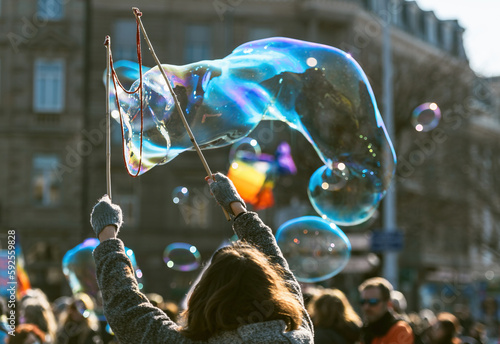 A group of people are creating huge, bright soap bubbles in mid-air with a bubble wand, marveling at the fragility and beauty of these liquid creations blowing in the air.
