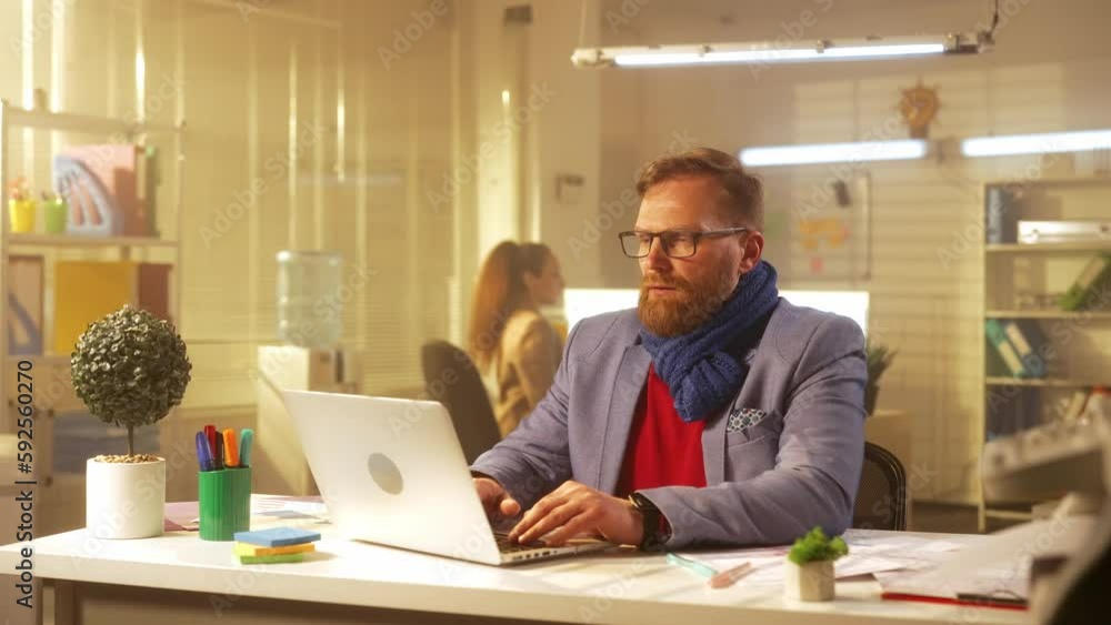 A middle aged man is typing on a laptop keyboard and suffers from fever and sore throat. A sick businessman with a scarf around his neck works in the office at the table. A middle aged man is typing on a laptop keyboard and suffers from fever and sore throat. A sick businessman with a scarf around his neck works in the office at the table.