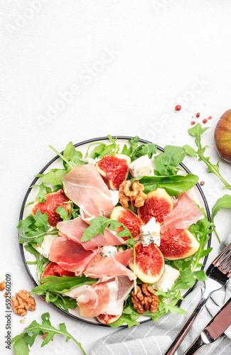 Summer salad with sweet figs, prosciutto, gorgonzola cheese, walnuts, arugula on white kitchen table background, top view, copy space