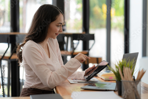 An Asian businesswoman using a digital tablet while sitting at a work desk in an office