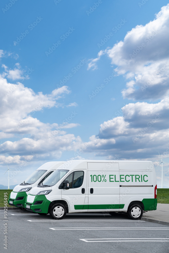 Electric vans parked in a row. Wind turbines in a horizon	