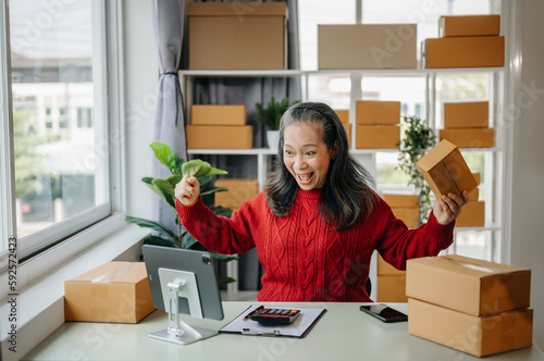 Senior business owner woman prepare parcel box and standing check online orders for deliver to customer on tablet, laptop Shopping Online concept. at home office. © Nuttapong punna