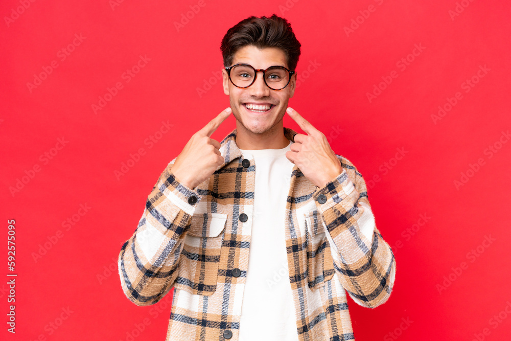 Fototapeta premium Young caucasian handsome man isolated on red background smiling with a happy and pleasant expression