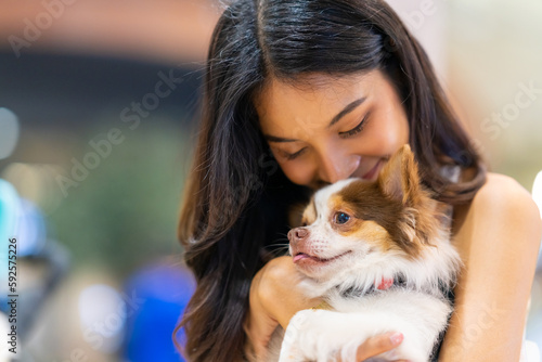 Asian woman playing with her chihuahua dog in cafe at pets friendly shopping mall. Domestic dog and owner have fun outdoor lifestyle travel city on summer holiday vacation. Pet Humanization concept.
