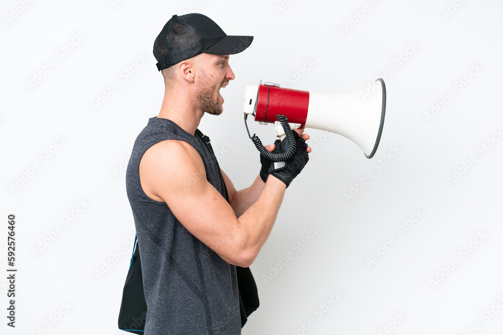 Young blonde sport caucasian man with sport bag over isolated white background shouting through a megaphone