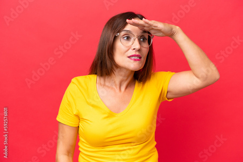 Middle-aged caucasian woman isolated on red background looking far away with hand to look something