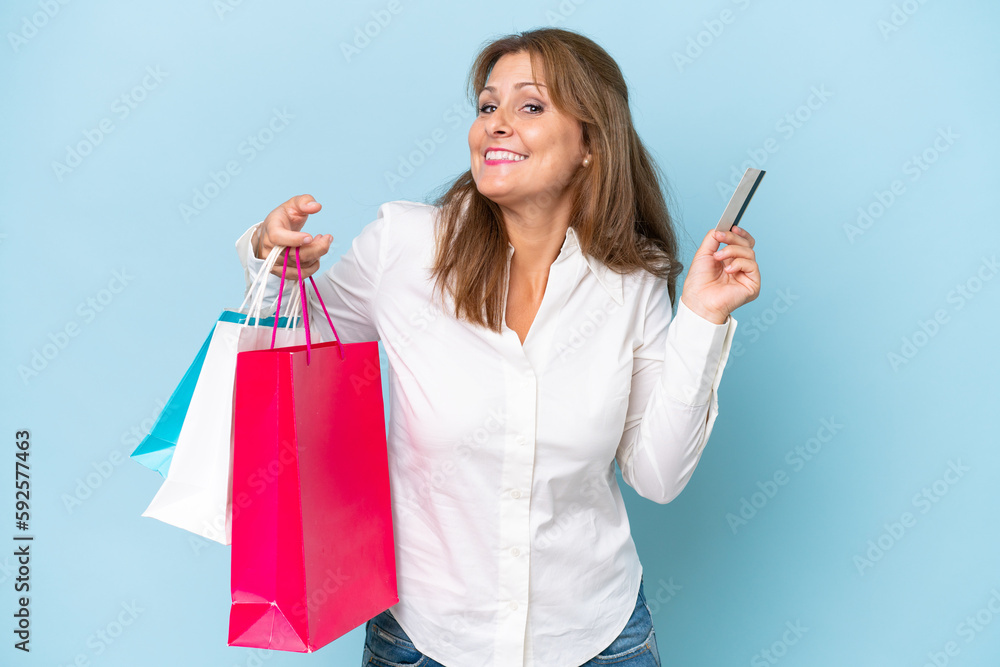 Middle-aged caucasian woman isolated on blue background holding shopping bags and a credit card Middle-aged caucasian woman isolated on blue background holding shopping bags and a credit card