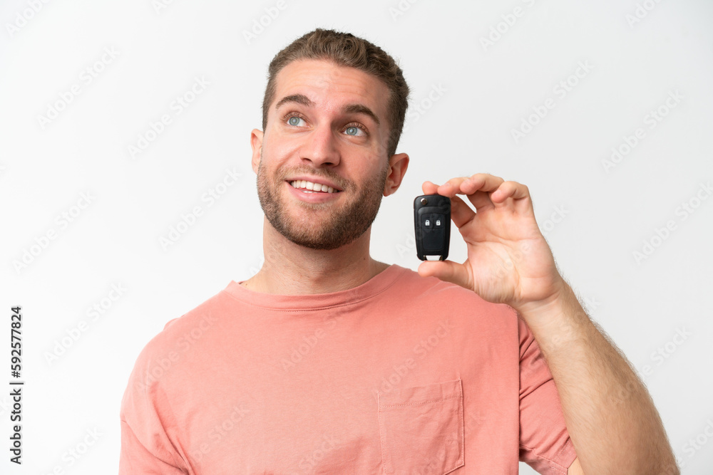 Young caucasian man holding car keys isolated on white background looking up while smiling Young caucasian man holding car keys isolated on white background looking up while smiling