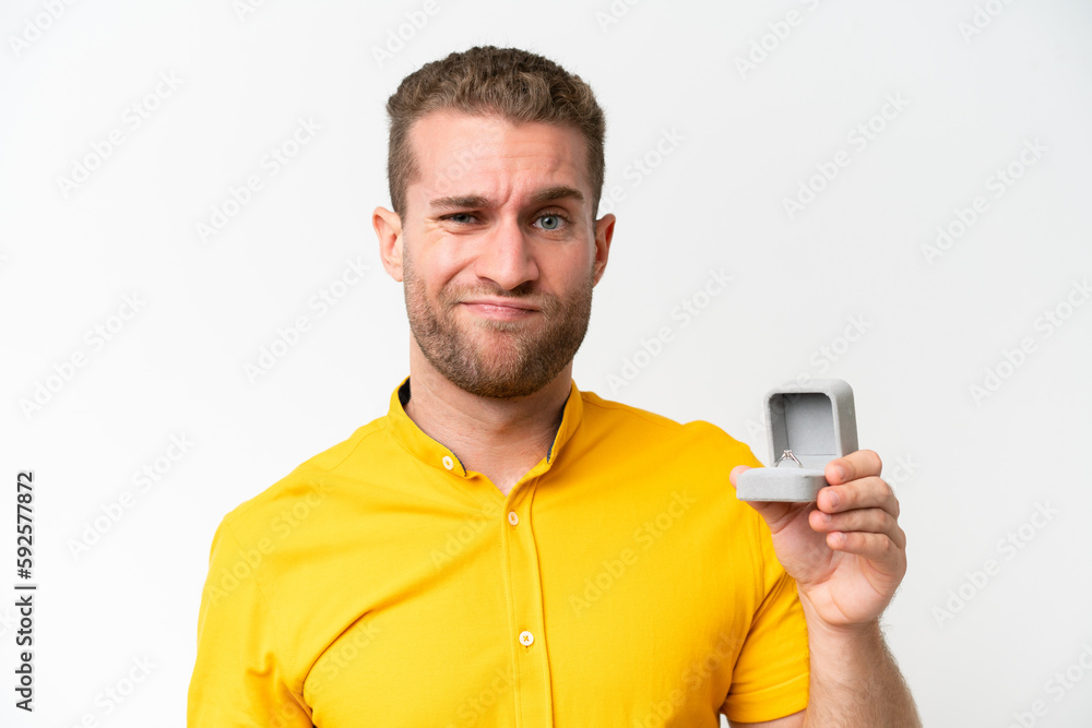 Young man holding a engagement ring isolated on white background with sad expression Young man holding a engagement ring isolated on white background with sad expression