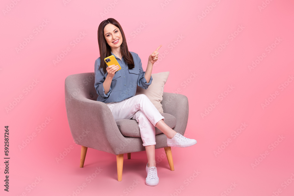 Full body photo of confident manager young lady sit chair direct finger mockup hold phone cheap phone accessories isolated on pink color background Full body photo of confident manager young lady sit chair direct finger mockup hold phone cheap phone accessories isolated on pink color background