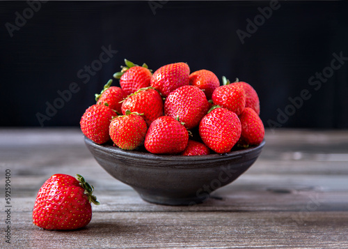Ripe garden strawberries in a vase on a wooden table.