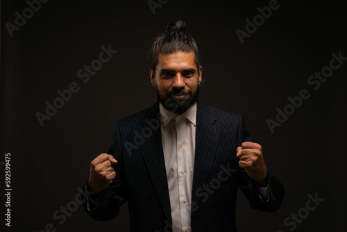 Hispanic elegant male with long hair in a suit with feast hands isolated on black background