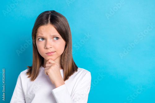 Photo of minded young girl with long hairstyle wear white long sleeve look empty space finger on chin isolated on blue color background