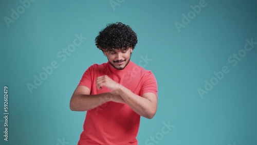 dancing young bearded Indian man 20s years old wearing coral t-shirt dance waving fooling around have fun enjoy isolated on a blue studio background