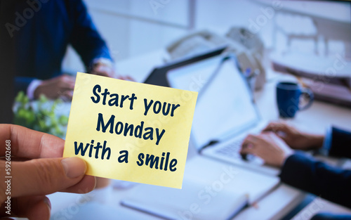 Male hand holding sticky note written Start your Monday with a smile.